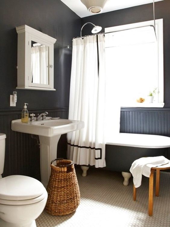 a chic modern country bathroom with black walls and paneling, white penny tiles, a black clawfoot tub, a vintage free-standing sink