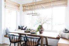 a chic modern country dining space with a built-in banquette seating, a stained table, black chairs and woven shades