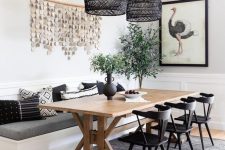 a chic modern farmhouse dining room with white paneled walls, a built-in banquette seating, a trestle dining table, black chairs and black woven pendant lamps