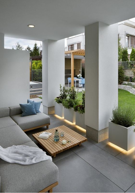 A chic modern porch in grey, with a sectional sofa, floating planters and built in lights