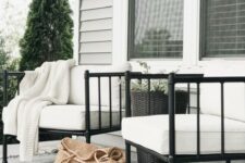 a chic modern porch with white soft chairs, a black tall planter with greenery, a monochromatic rug with fringe is welcoming