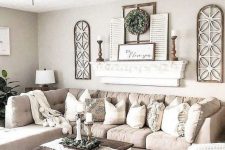 a chic neutral farmhouse living room with a tan sectional, a shelf with shutters and wooden candlesticks, a low coffee table