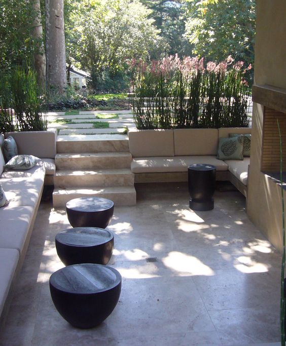 A contemporary sunken patio with a fireplace and built in upholstered benches, small coffee tables and grass around it is great for relaxing