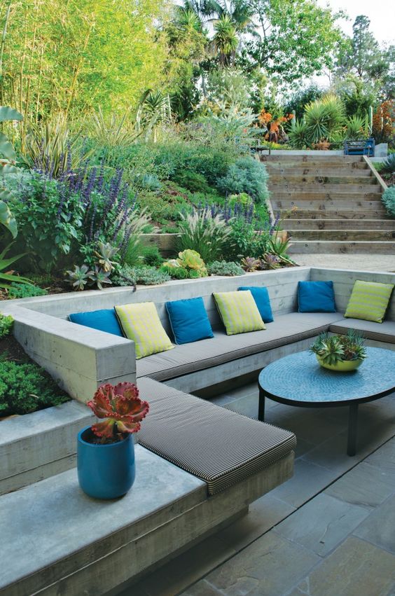 a contemporary sunken patio with built-in benches, colorful pillows and a coffee table plus greenery and blooms around