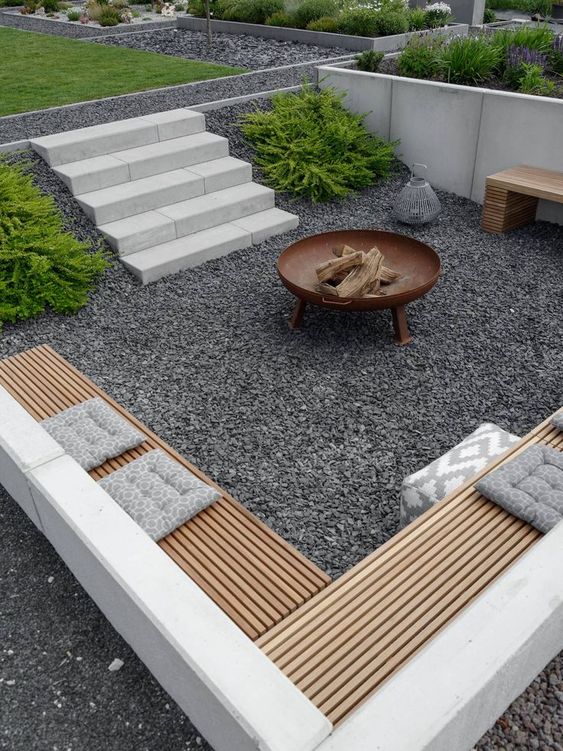 a contemporary sunken patio with gravel on the ground, built-in benches and a fire pit is amazing for spending nights here