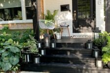 a contrasting modern porch with a black floor and ladder, white chairs, a side table, black candle lanterns and potted greenery