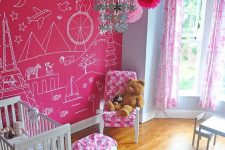 a cool kid’s room with a hot pink accent wall, a crib and a comfy chair with a pouf, a white dining space and a floral chandelier