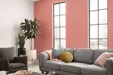 a cool modern living room with a pink accent wall, a grey sofa and colorful pilows, a black coffee table and a catchy chandelier