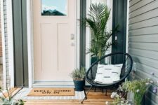 a cool modern porch with a blush door, a black chair, potted plants and blooms and layered rugs is a cool and chic space