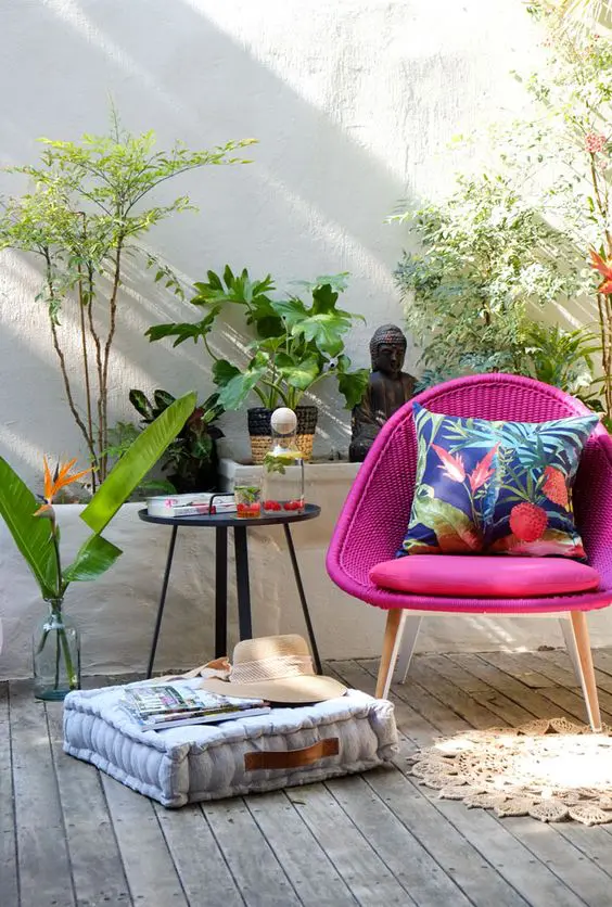 A cool outdoor nook with a woven hot pink chair, a side table, a cushion, potted plants and beautiful Asian inspired decor
