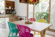 a crazy boho eat-in kitchen with whitewashed furniture, a shabby trestle table, a hot pink, turquoise, yellow and red chair and a jaw-dropping pendant lamp