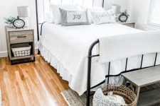 a dreamy farmhouse bedroom with a forged bed, wooden nightstands, a wooden bench and a basket for storage, some greenery