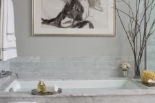 a fancy bathroom with grey marble tiles and marble itself, a crystla chandelier and a bold statement artwork just wows