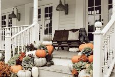 a farmhouse fall porch with a black bench and lots of pillows, pumpkins, blooms and greenery and vintage sconces on the walls