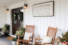 a farmhouse porch styled for summer, with wooden rockers, potted plants, a sign and a rug is a very welcoming and cool space