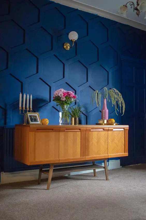 a gorgeous navy hexagon panel accent wall, a stained vintage dresser, some greenery and blooms and elegant candles in a candle holder