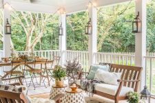 a large and welcoming farmhouse porch with a simple wooden dining set, wooden benches with upholstery, side tables and potted plants