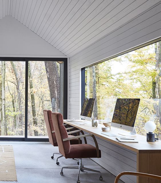 a lovely and clean shared modern country home office with white planked walls and a shared desk plus glazed walls for views