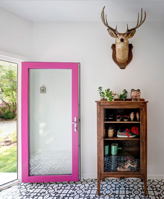 a lovely and quirky entryway with a mosaic tile floor, a vintage wooden cabinet, a door with a hot pink frame and taxidermy