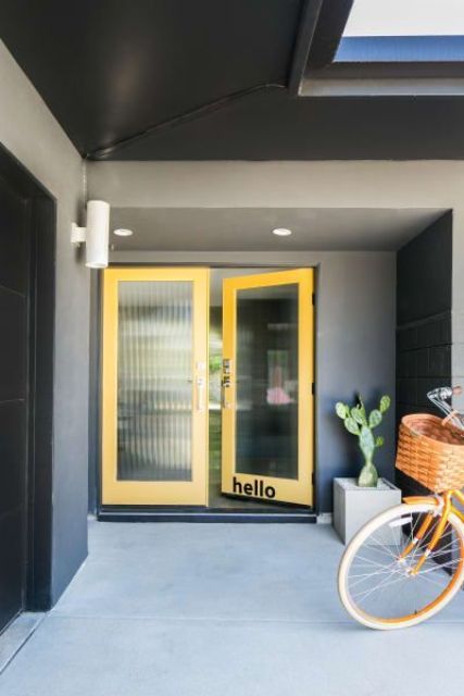 A lovely mid century modern entrance with grey walls and yellow doors with reeded glass, a potted cactus and a bike