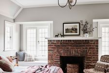 a lovely modern country bedroom with windowsill daybeds, a fireplace clad with bricks, a bed and a printed chair feels cozy and inviting