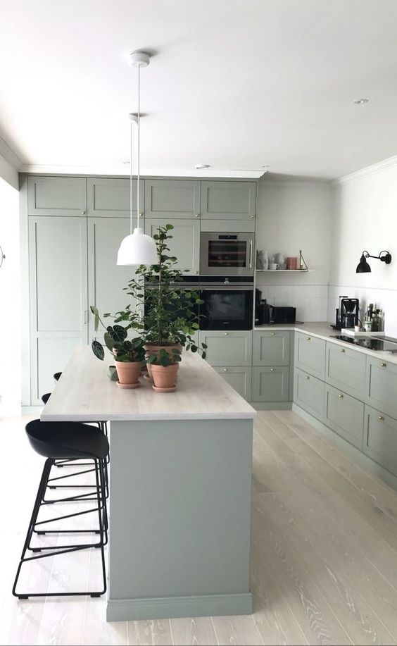 a lovely pale green modenr country kitchen with neutral countertops and tall black stools and sconces is a chic room