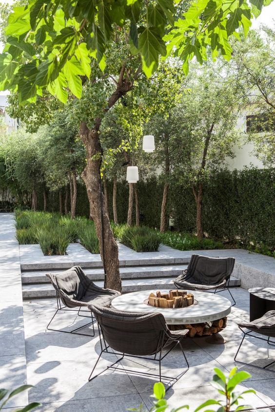 a lovely sunken outdoor space fully clad with tiles, with a round fire pit, some upholstered chairs and a living wall
