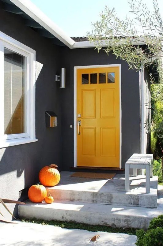 a marigold door with glass panes makes a bold statement with graphite grey walls around and orange pumpkins on the steps is a cool modern solution