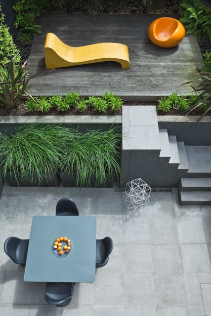 a minimalist outdoor space with a raised platform with a lounger and a fire pit and a dining space plus growing grasses around