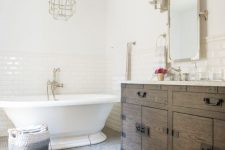 a modern French country bathroom with subway and penny tiles, a stained vanity, a vintage tub and a faceted lamp plus gold touches