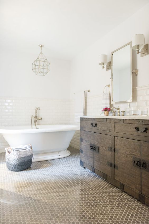 a modern French country bathroom with subway and penny tiles, a stained vanity, a vintage tub and a faceted lamp plus gold touches