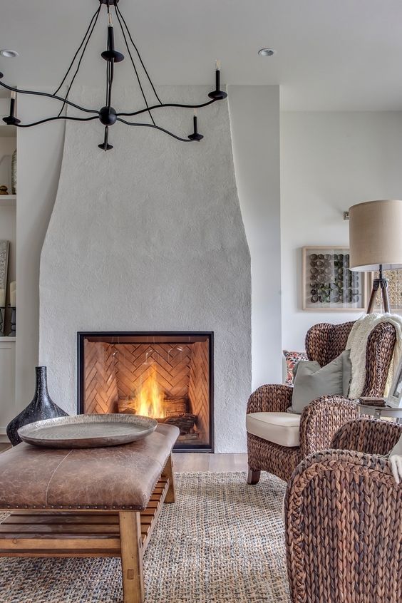 a modern French country living room with a large fireplace, a leather ottoman as a table, woven chairs and a jute rugs looks unique