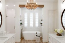 a modern country bathroom with a laminate floor, white walls, elegant white shaker style vanities and cool white appliances plus a wooden chandelier