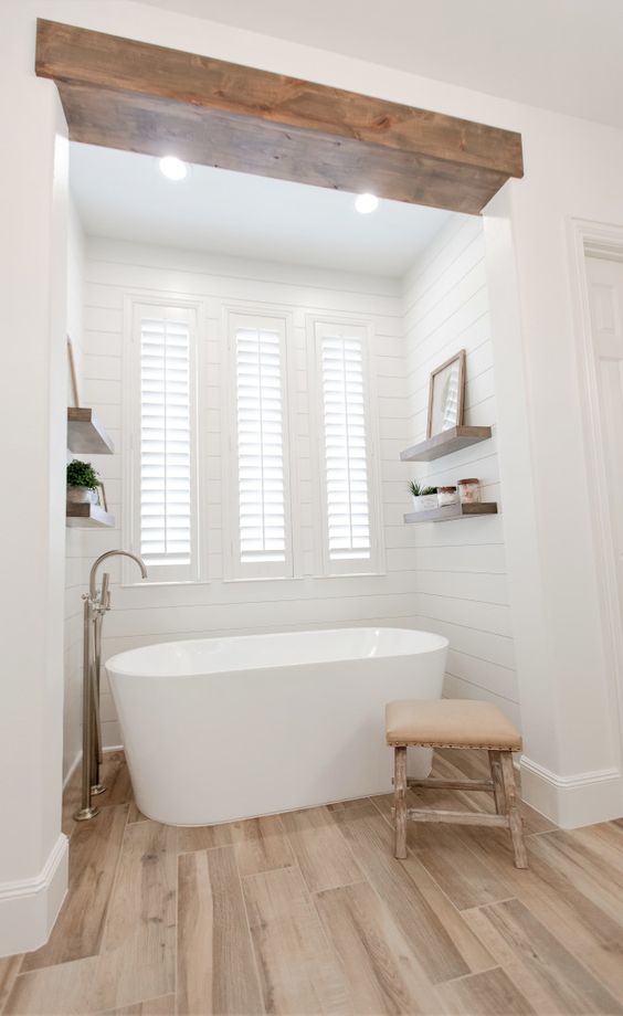 a modern country bathroom with white planked walls and laminate on the floor, a wooden beam, a bay window and a lovely bathtub