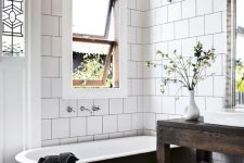 a modern country bathroom with white square and bright mosaic tiles, a black clawfoot tub, a dark stained vanity, pendant lamps and greenery