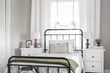 a modern country bedroom with a forged bed and white nightstands, baskets and a woven rug, neutral textiles and plants