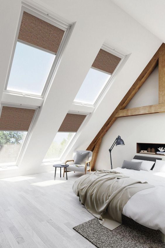 A modern country bedroom with an attic ceiling and lots of windows, wooden beams and a built in fireplace, cool furniture and a sitting nook by the window