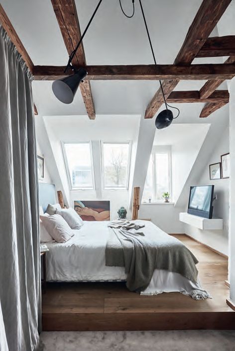 a modern country bedroom with dark stained wooden beams, a large bed and some artworks plus a TV on a stand is welcoming