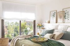 a modern country bedroom with natural touches, a ledge with artworks, a bed with green and white bedding and a large window