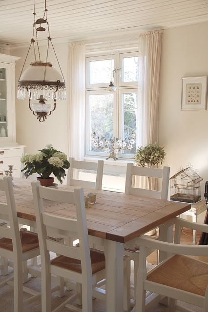 a modern country dining space with a simple wooden dining set, a large white buffet, a vintage chandelier and neutral textiles