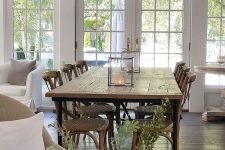 a modern country dining space with a stained table and chairs with woven seats, a vintage chandelier and cadle lanterns