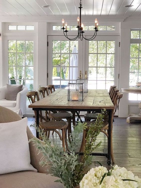 a modern country dining space with a stained table and chairs with woven seats, a vintage chandelier and cadle lanterns