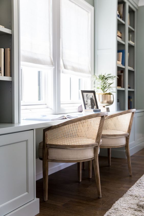 a modern country home office with a large built-in shelving unit that includes a double desk and rattan chairs