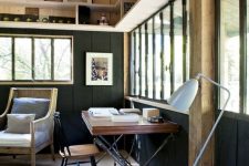 a modern country home office with wooden beams, black planked walls, a cool desk and a vintage chair, a rattan chair and a floor lamp