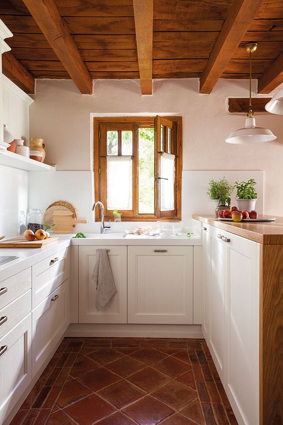 a modern country kitchen with a tiled floor, white cabinets and a raised butcherblock countertops, a wooden ceiling with beams and frames on the window