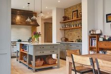 a modern country kitchen with exposed brick, white subway tiles, light grey cabinets and a kitchen island, pendant lamps and metallic fixtures