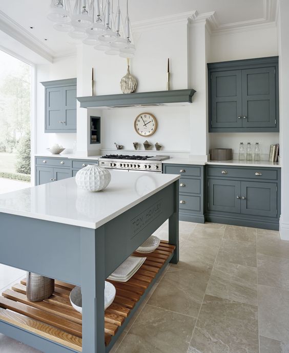 A modern country kitchen with graphite grey cabinets and a kitchen island, white countertops and a built in hood plus a glazed wall