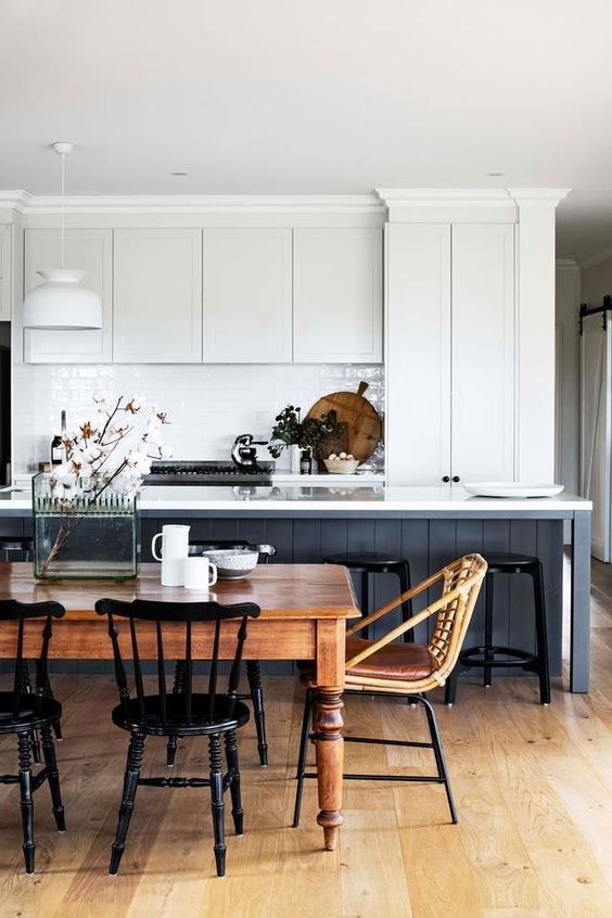 a modern country kitchen with white cabinets and a navy kitchen island, a vintage table and chairs for the dining space