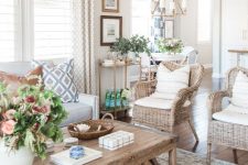 a modern country living room in neutrals, with a creamy sofa, woven chairs, a low coffee table, printed textiles and potted plants