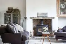 a modern country living room with a hearth, graphite grey furniture, a coffee table and a pouf, some vintage storage units